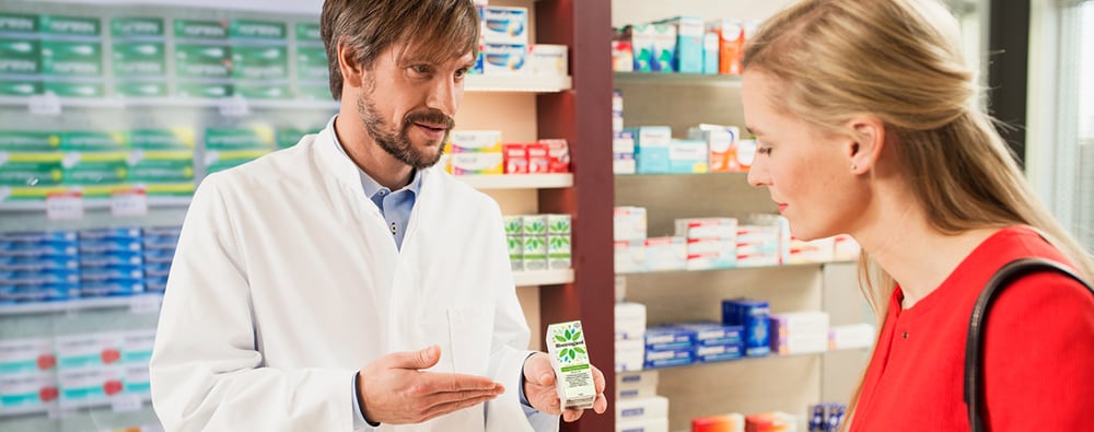Žena u crvenom džemperu kupuje Iberogast od farmaceuta u ljekarni.